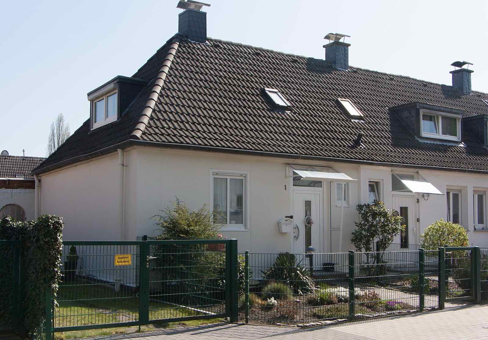 Helles Reihenhaus mit Gauben und kleinem Vorgarten hinter einem grünen Zaun